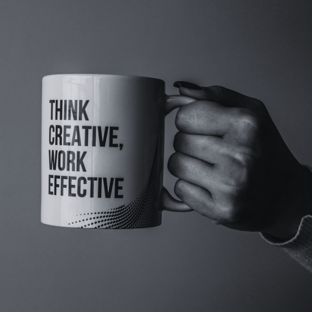 Black and white photo of mannicured hand holding a mug with 'think creative, work effective' slogan